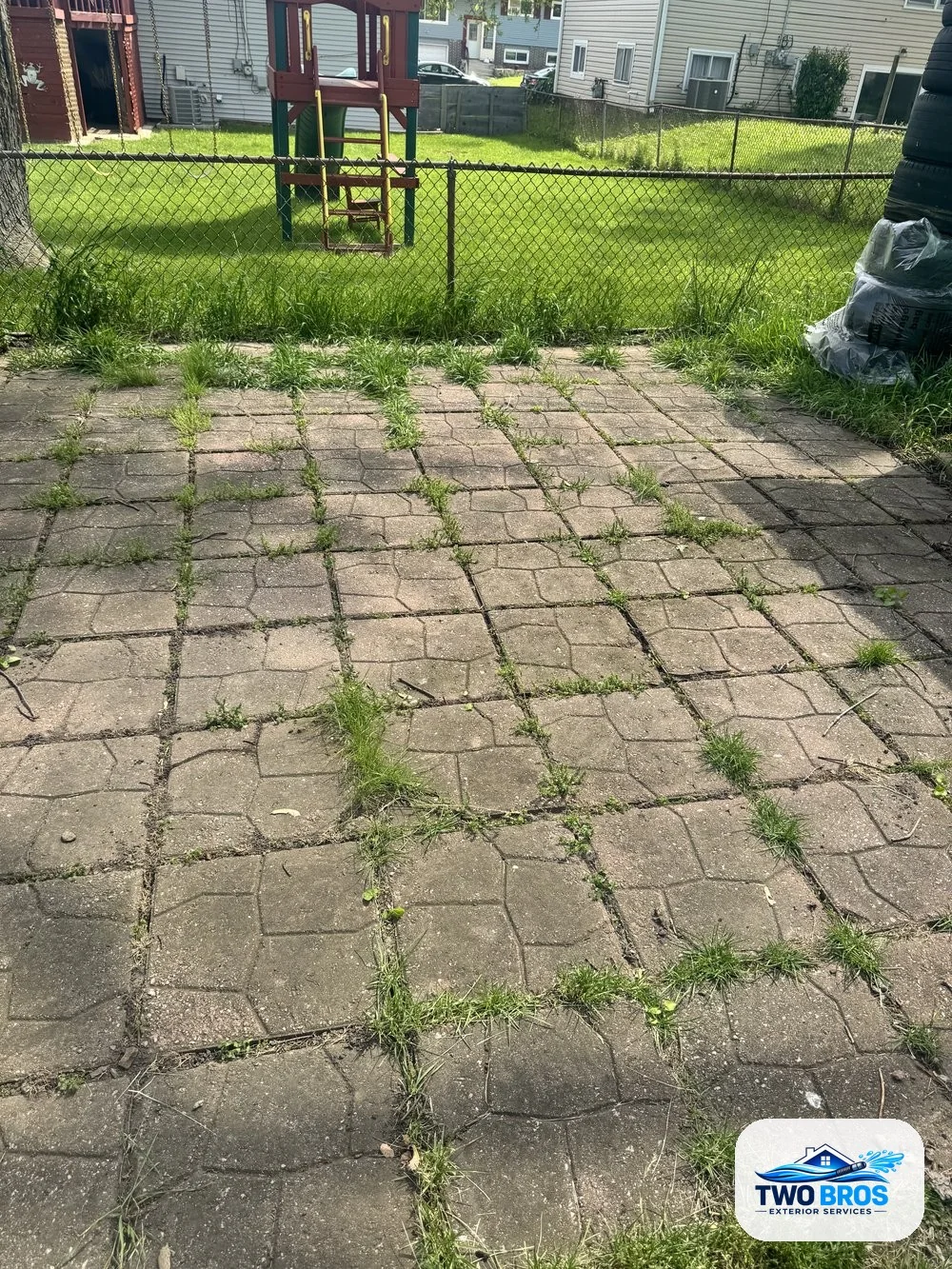 Paver patio before cleaning, furniture removed, showing dirt and weeds between pavers